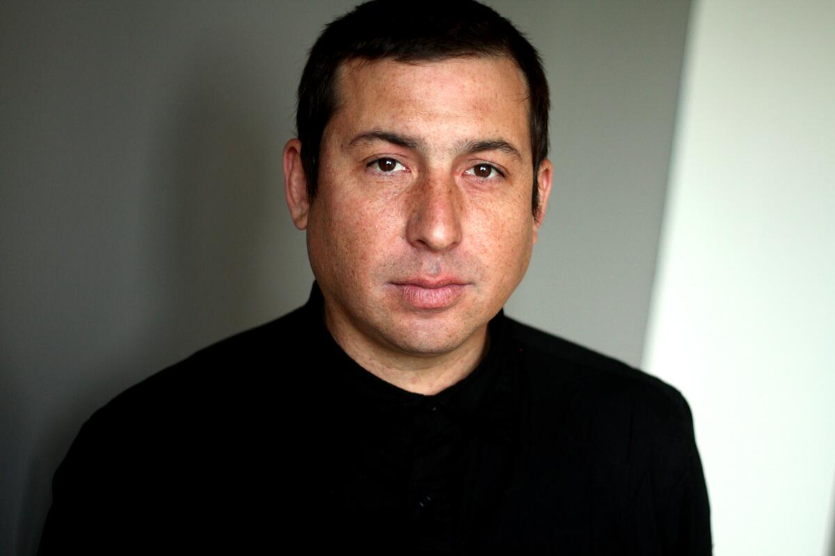 Author Tommy Orange, in a black shirt, looks straight at the camera.