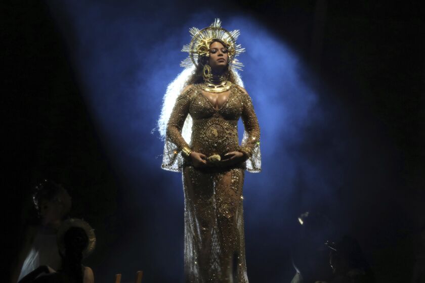 A woman posing on a stage in a sheer gold dress and an elaborate crown