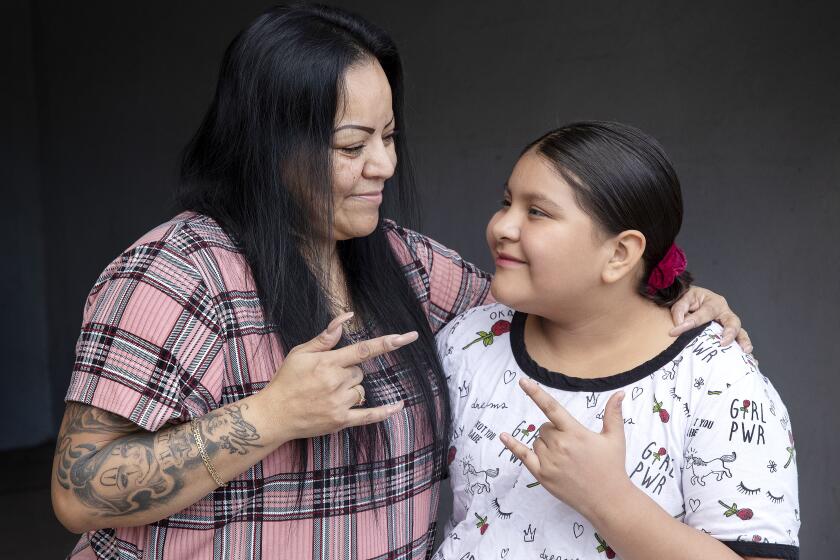 CANOGA PARK, CA - November 22, 2021: Rena Tafoya, 48 and her daughter, Maya Flores, 11, who is a deaf student enrolled in LAUSD'S City of Angels independent study program, are photographed in front of their home in Canoga Park. They are signing, "I Love You," to each other, something they do every night before going to bed. Rena tried to get her daughter an ASL interpreter, but it took more than 2 months. Children like Maya, who require services under their Individualized Education Plan, are being left behind by independent study programs, which became the only official distance learning program this year. (Mel Melcon / Los Angeles Times)