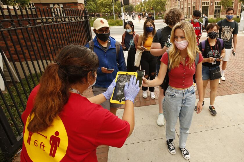 LOS ANGELES, CA - AUGUST 23: USC CARE Crew Team Ambassador Lesly Plancarte, left, uses the iPad to check the QR code as USC students, faculty and visitors use their phones to display their "Trojan Check" QR code scanned by a QR reader or iPad at various campus gates in order to access the USC campus Monday for the first day of in-person classes. USC and California State University campuses start in-person classes on Monday, serving as a test case for whether vaccine mandates, masking, regular testing and other protocols can minimize spread of the Delta variant even as thousands of students congregate in classes, dorms and social events. USC campus on Monday, Aug. 23, 2021 in Los Angeles, CA. (Al Seib / Los Angeles Times).