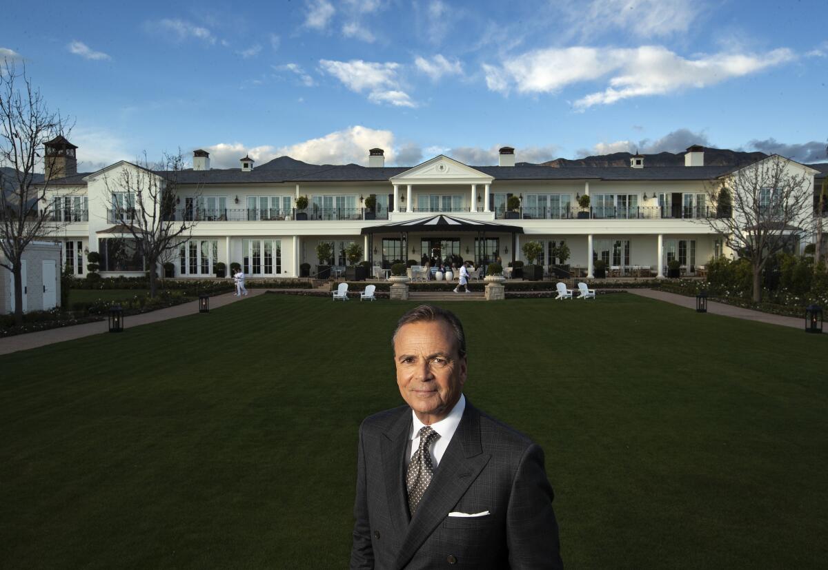 A man stands on an extensive lawn in front of large white building.