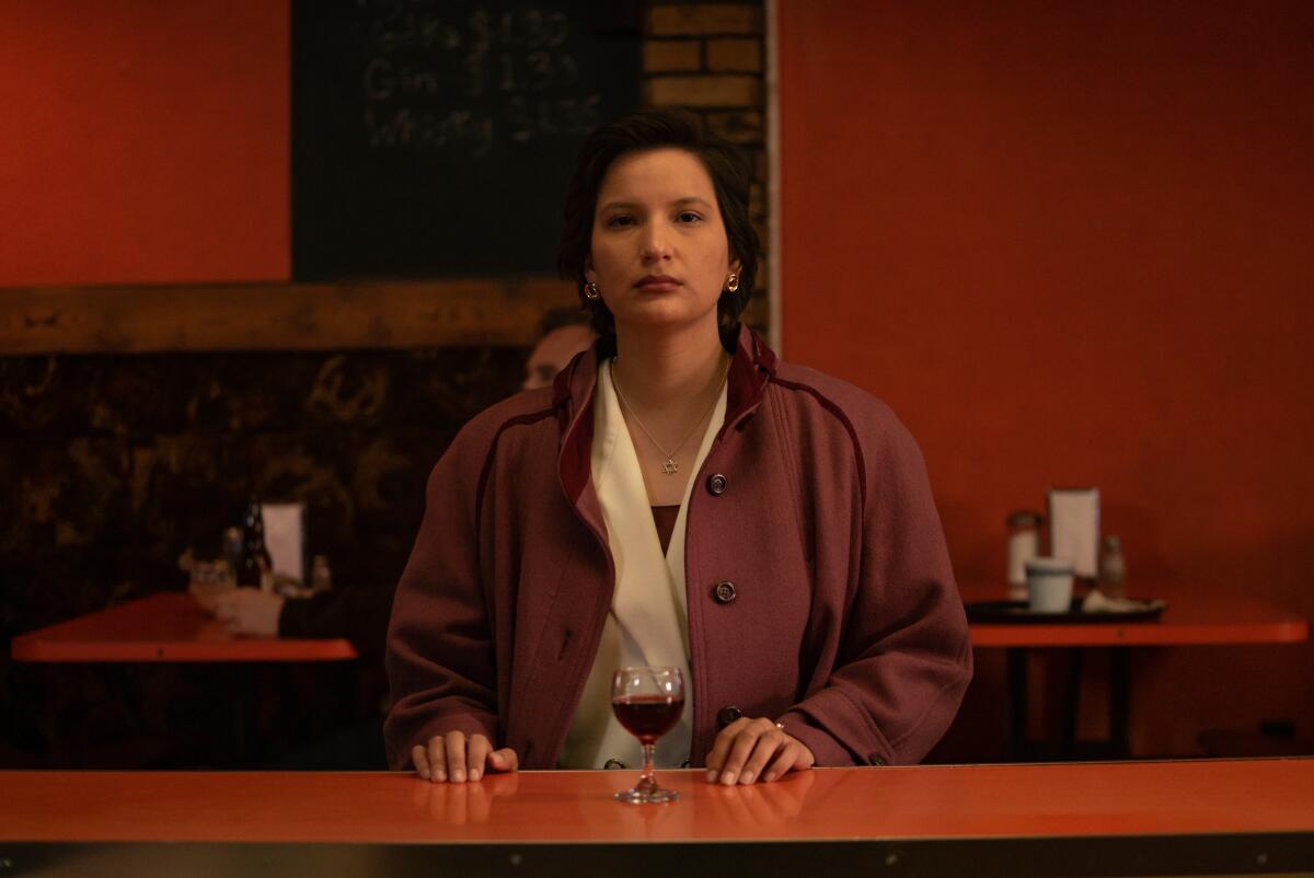 A woman stands at a bar with a wine glass in front of her.