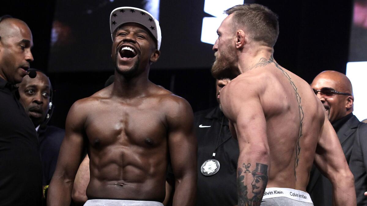 Floyd Mayweather Jr. has a laugh as Conor McGregor glares at him after each fighter weighed in Friday.