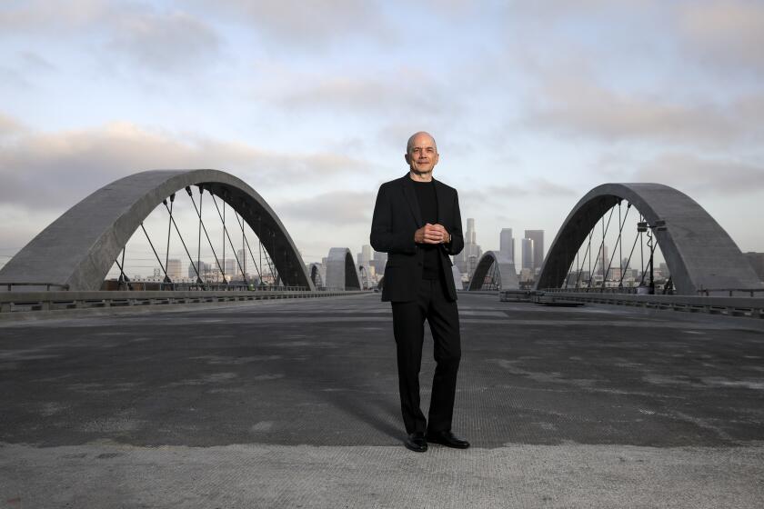 Michael Maltzan, in a black suit, stands on the deck of the under-construction 6 Street Viaduct in Los Angeles