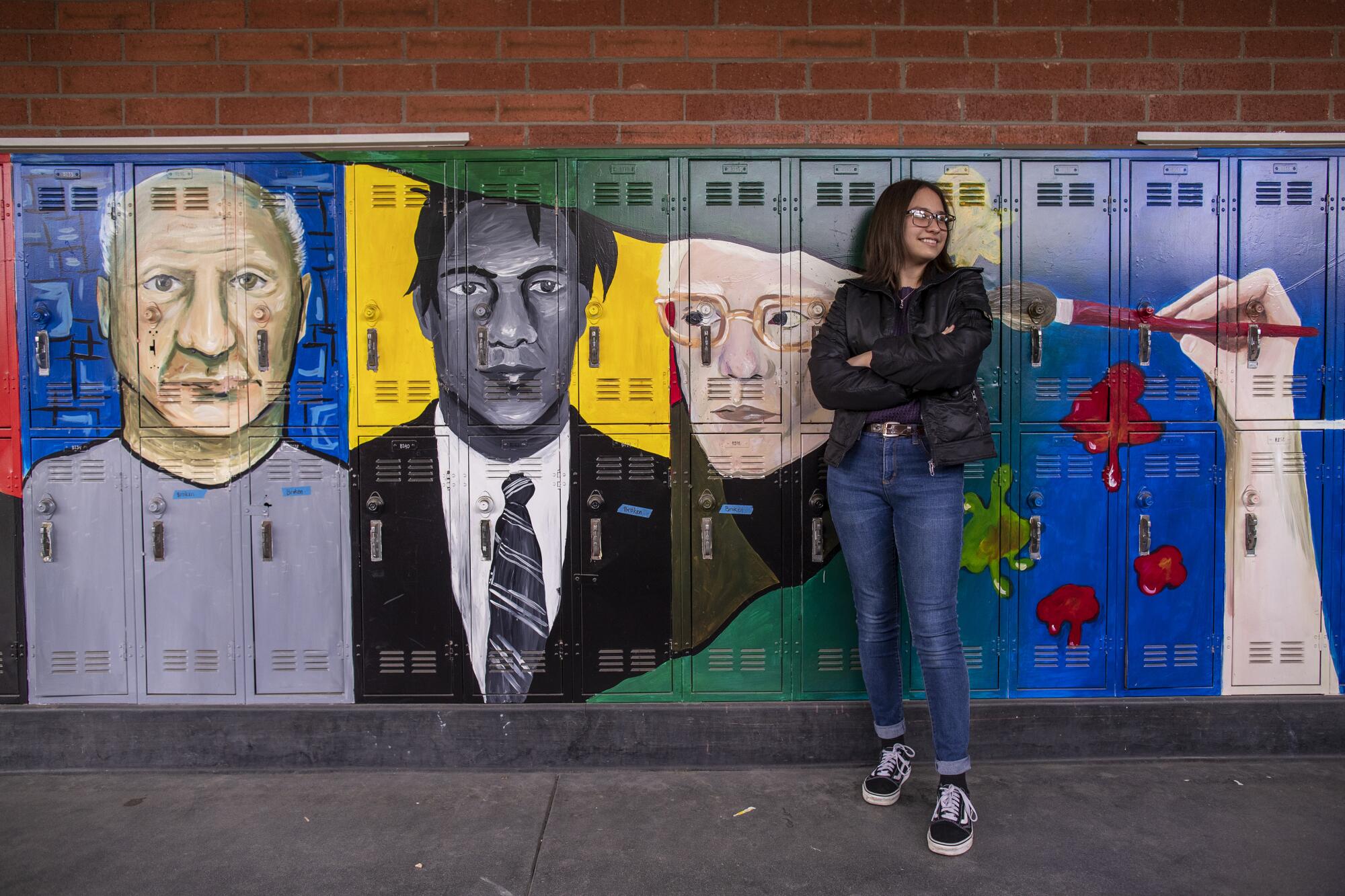 A student poses in front of lockers with a mural on them