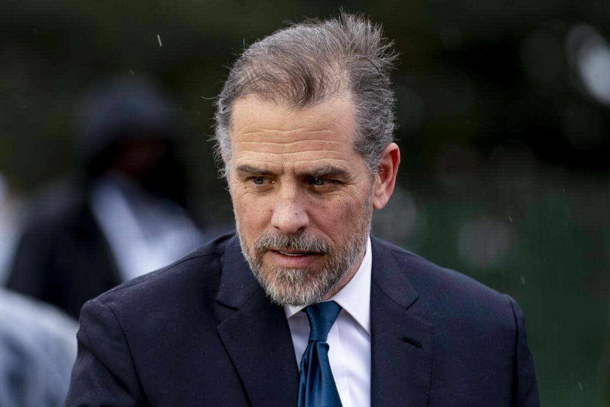 A man with graying hair and beard, in a dark suit and blue tie