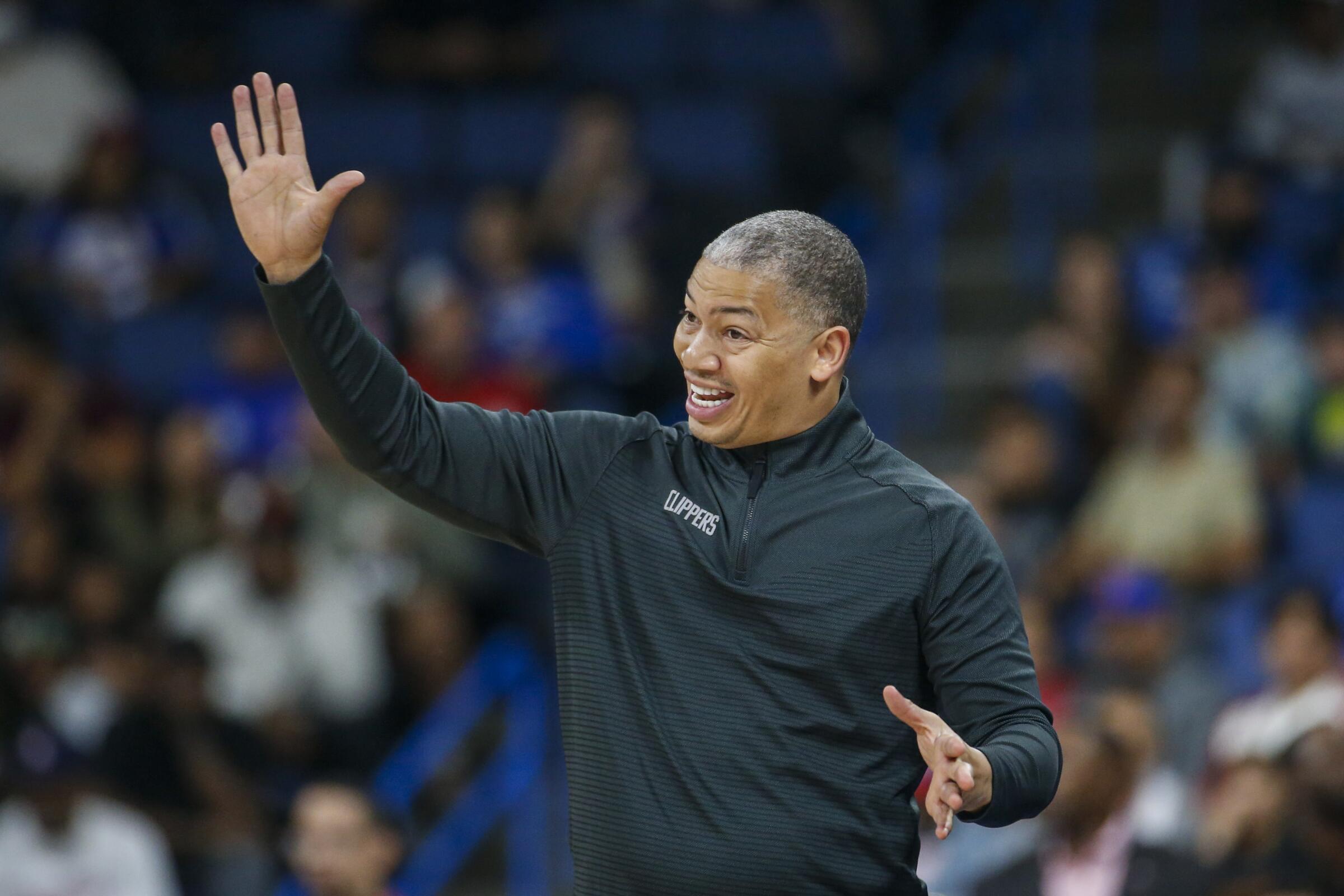 Clippers coach Tyronn Lue raises his right arm while calling out instructions to his players on the court.