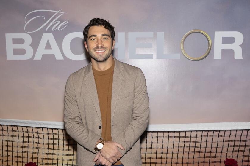 'The Bachelor' star Joey Graziadei smiles in front of a Bachelor TV show poster