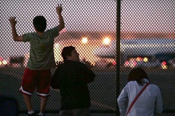 Onlookers climb a fence to get a better view of cleanup efforts after the Airbus A320 made its emergency landing at Los Angeles International Airport.