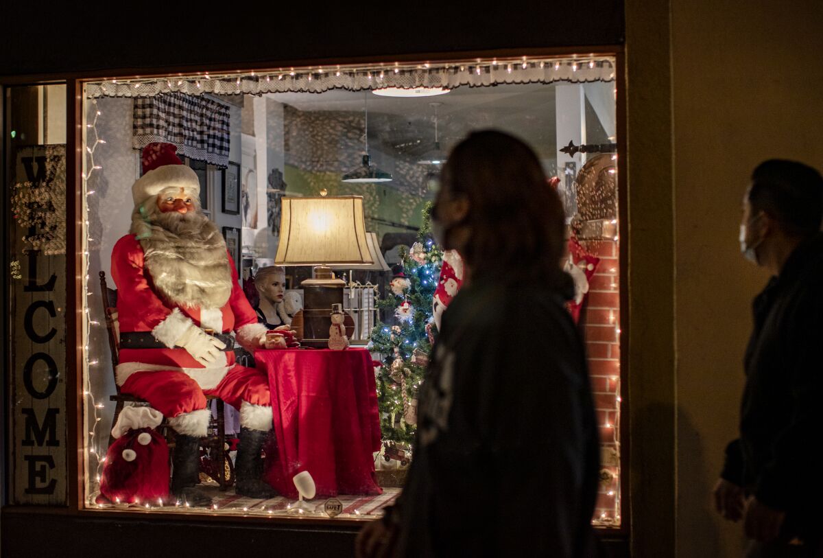 Wearing face masks, people pass by a Christmas-themed store window