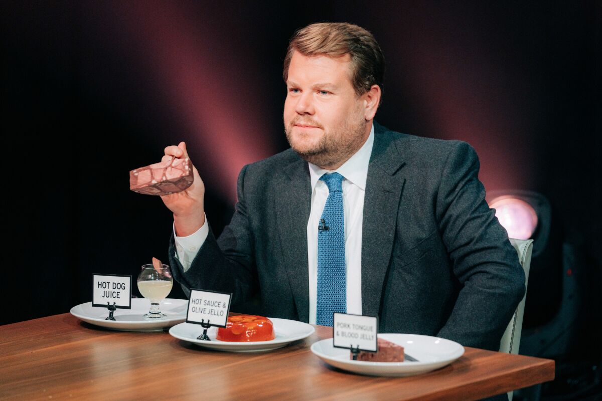 A man in a suit sits at a table with three plates of food with labels set in front of him