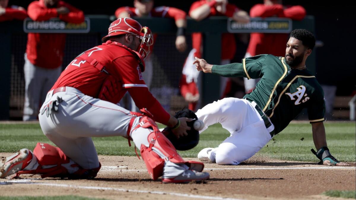 Oakland Athletics shortstop Marcus Semien, right, scores past Los Angeles Angels catcher Kevan Smith on a two-run double by Stephen Piscotty during the first inning of Tuesday's exhibition game.