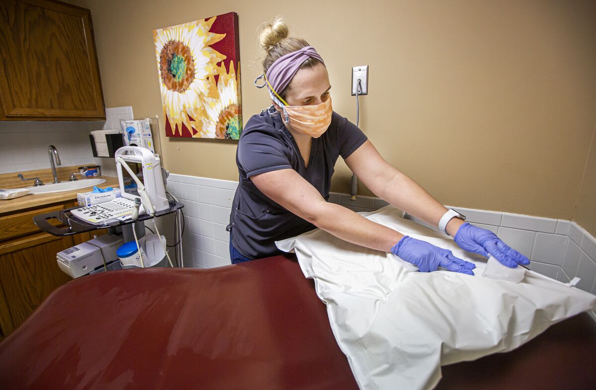 A person wearing scrubs and gloves disinfects an examining room