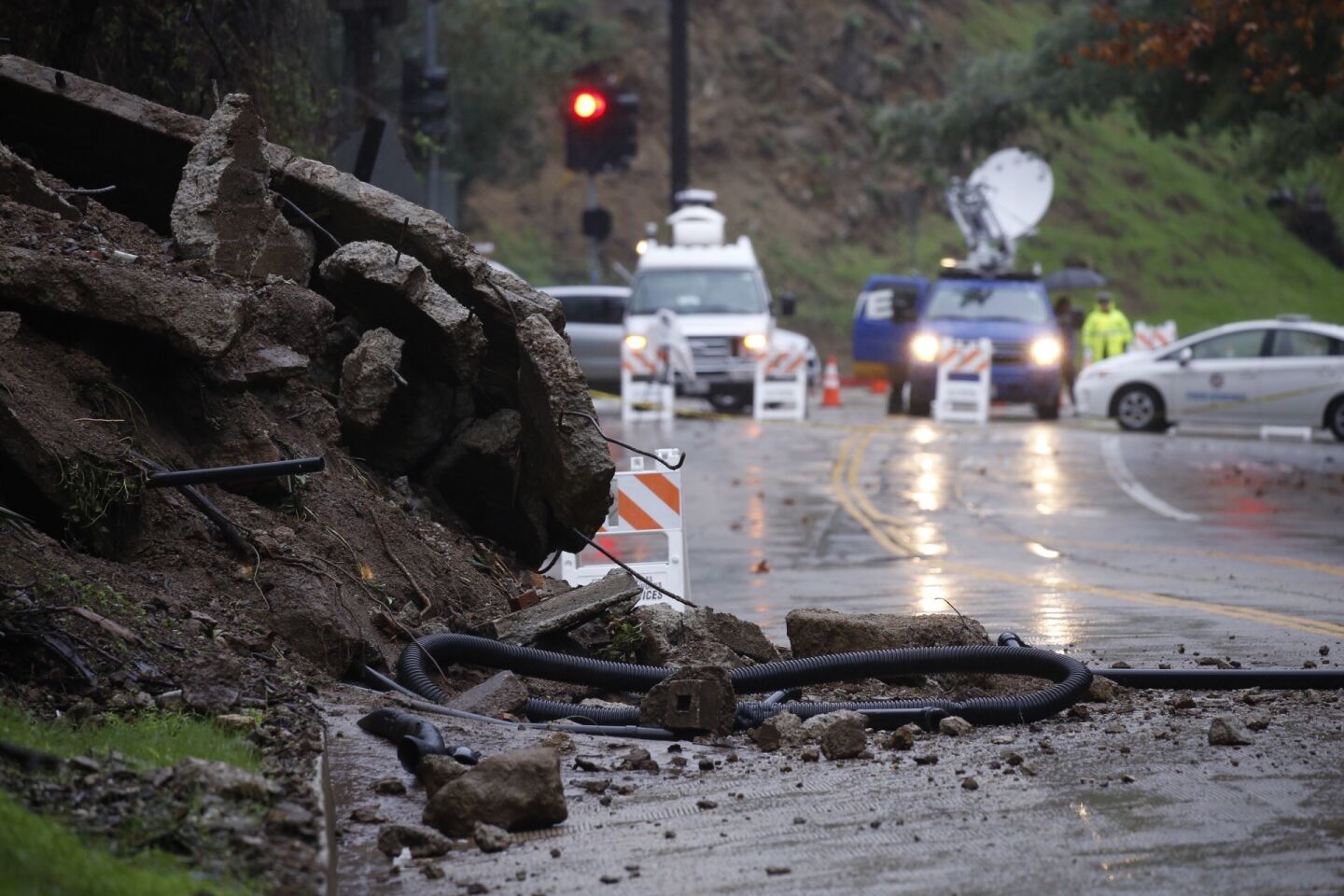 News crews gather on Laurel Canyon Blvd, which remained closed in both directions Thursday morning in the Hollywood Hills when part of a home's concrete foundation tumbled down a hillside after a round of rainfall.