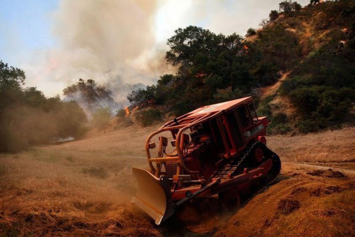 A fire tractor digs a trench to slow down the fire raging in Monrovia near homes April 20, 2013. Firefighting airplanes were called in to protect homes on the northwestern side of Monrovia today, as a brushfire covering 18 acres sent a huge cloud into the sky just 1-1/2 miles from a big crowd at Santa Anita Race Track. Twenty-five fire trucks, about 125 firefighters and several helicopters were working to protect homes on the urban boundary in the wildlands of the steep San Gabriel Mountain foothills, adjacent to subdivisions and hillside homes in Arcadia and Monrovia, Monrovia fire chief Chris Donovan said. At 2 p.m., Monrovia firefighters began evacuating several neighborhoods, including the Heather Heights, Alta Vista, Melrose, Patricia Way, Hidden Valley, Mesa Circle and Sky Way areas. The fire chief said winds were light, but those winds normally shift direction in the afternoons in the foothills, and 15 additional engines were being called in for structure protection. Residents were being sent to a shelter at the Monrovia Public Library, at Myrtle and Palm avenues.