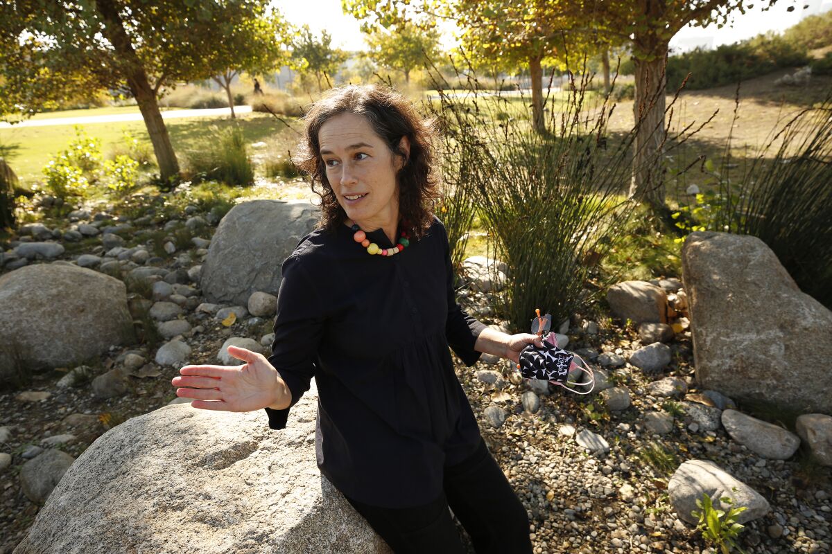 A woman gestures while talking amid landscaping at a park