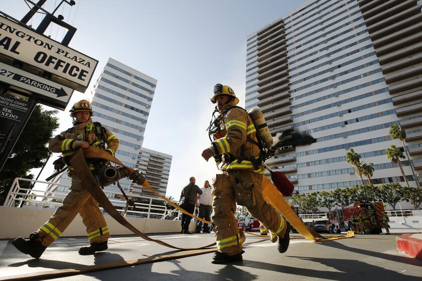 LOS ANGELES, CA - JANUARY 29, 2020 Firefighters run to complete hose lays for water as they battle a large blaze that has enveloped the sixth floor of Barrington Plaza, a 25-story Westside residential building in the 11700 block of Wilshire that errupted at 8:30 AM Wednesday morning. (Al Seib / Los Angeles Times)