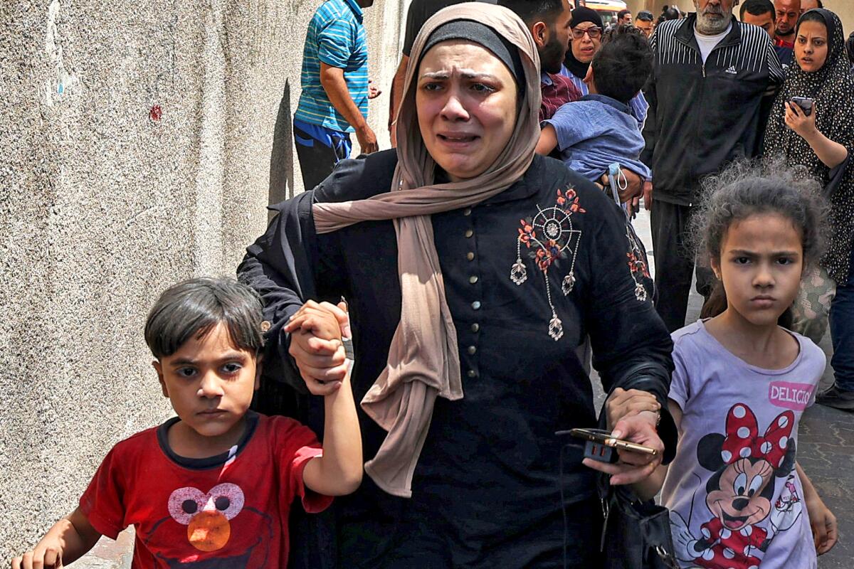 A woman with a distraught expression holds the hands of two young children as they hurry amid a crowd
