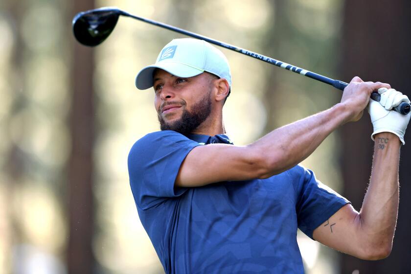 In a waist-up horizontal frame, Stephen Curry looks to the left while pausing in an upward seeing with a golf club.