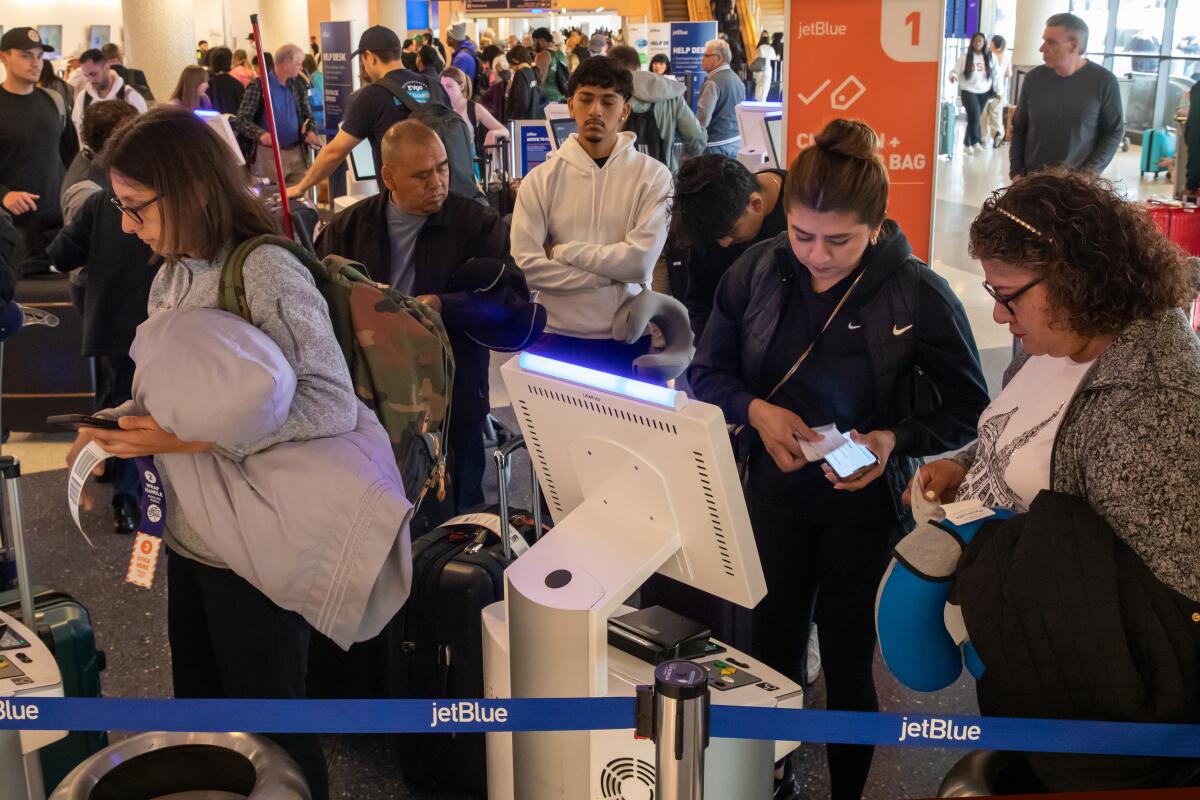 People with luggage line up at ticketing kiosks in an airport