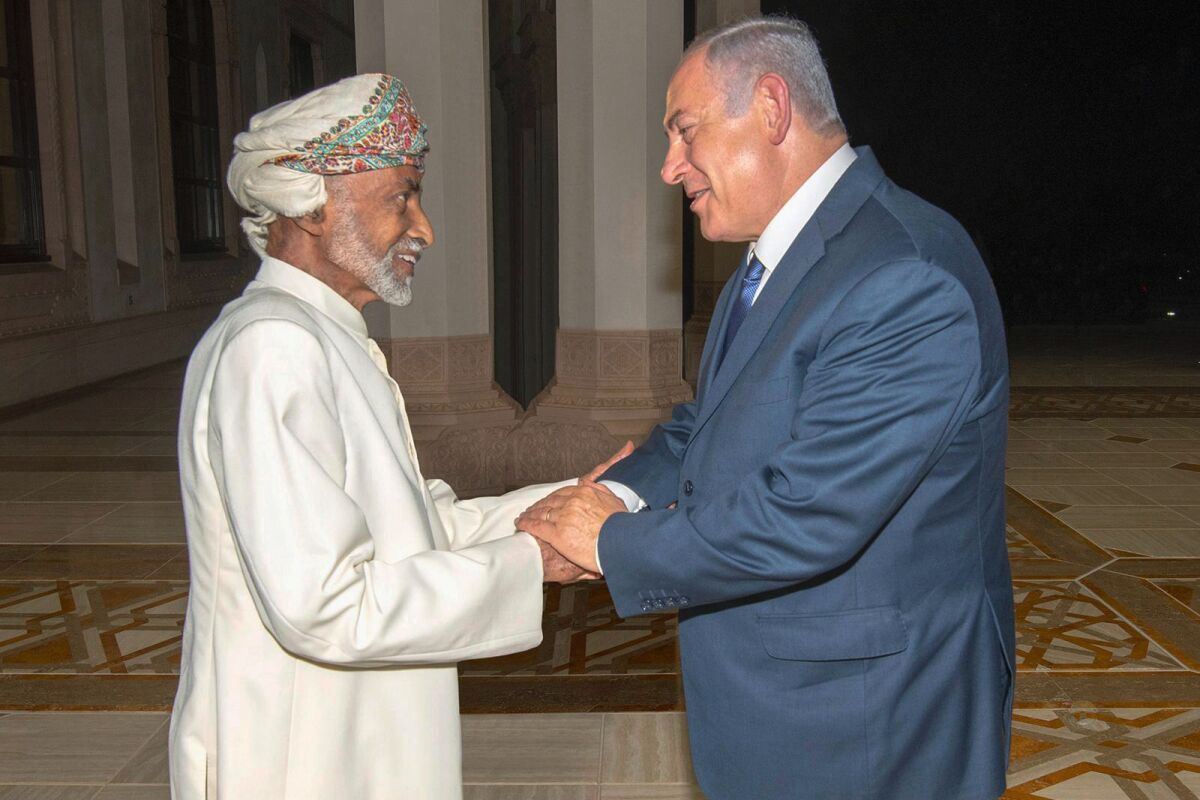 Sultan Qaboos bin Said Al Said, left, shakes hands with Benjamin Netanyahu while facing him. Both are smiling.