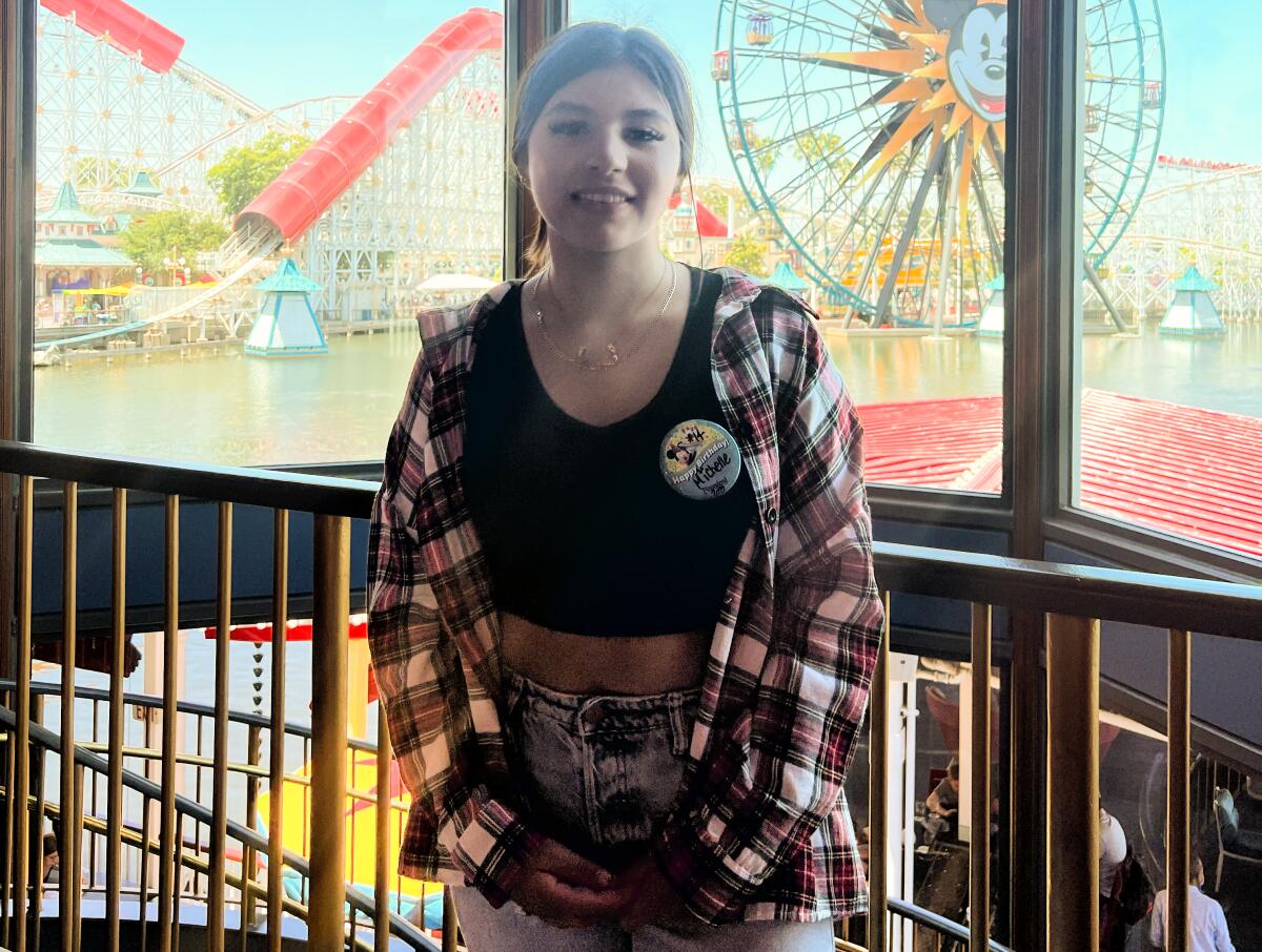 A teenage girl poses for a picture with a roller coaster and Ferris wheel in the background