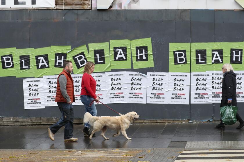 People walk past posters placed by climate activists ahead of a protest march by them through the streets of Glasgow, Scotland, Friday, Nov. 5, 2021 which is the host city of the COP26 U.N. Climate Summit. The protest was taking place as leaders and activists from around the world were gathering in Scotland's biggest city for the U.N. climate summit, to lay out their vision for addressing the common challenge of global warming. (AP Photo/Scott Heppell)