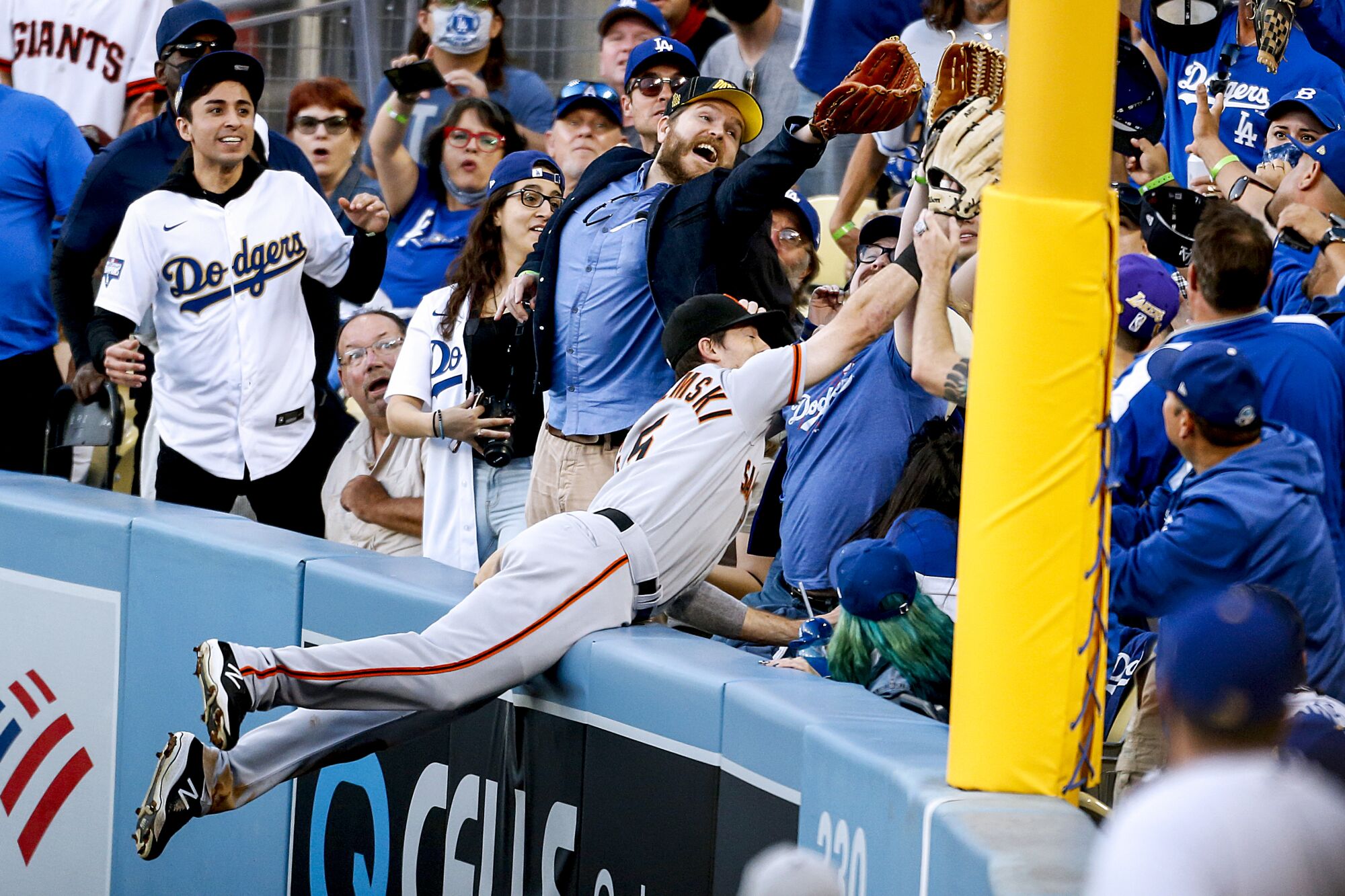 A baseball player dives into the stands after a ball, surrounded by fans, a couple of whom also try to catch the ball.