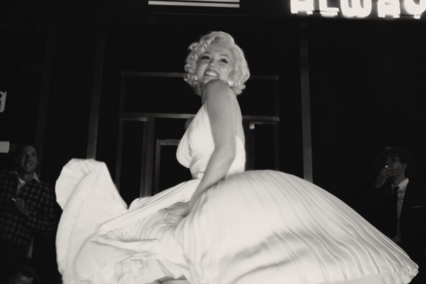 A black-and-white image of a blond woman posing in a billowing, white dress