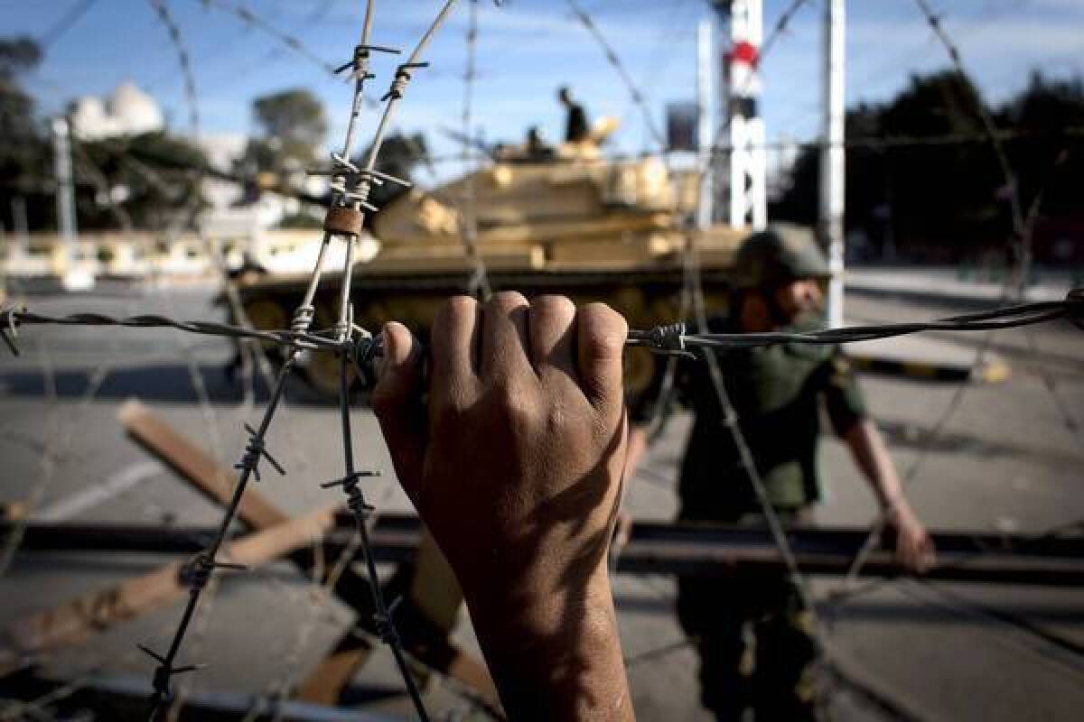 Barbed wire and tanks surround the presidential palace in Cairo, while protesters outside the barrier chant slogans against President Mohamed Morsi.