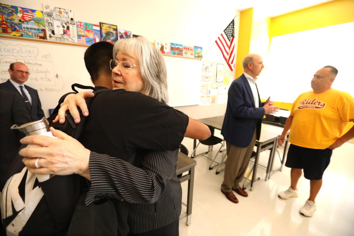 A woman hugs a student in a classroom