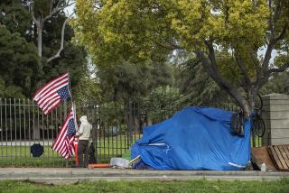 LOS ANGELES, CA-APRIL 6, 2020: A man pauses to straighten up a flag pole at its base, while walking past a homeless encampment on San Vicente Blvd in Los Angeles, located just outside the grounds of the VA West Los Angeles Campus. The VA is opening the campus to camping by by homeless veterans in a designated parking lot and also 2 sprung shelters that will have 25 beds in each. The VA had long camping or more interim housing on the 388 acre campus, saying vets had ample shelter space but Covid-19 pandemic reversed that position. (Mel Melcon/Los Angeles Times)