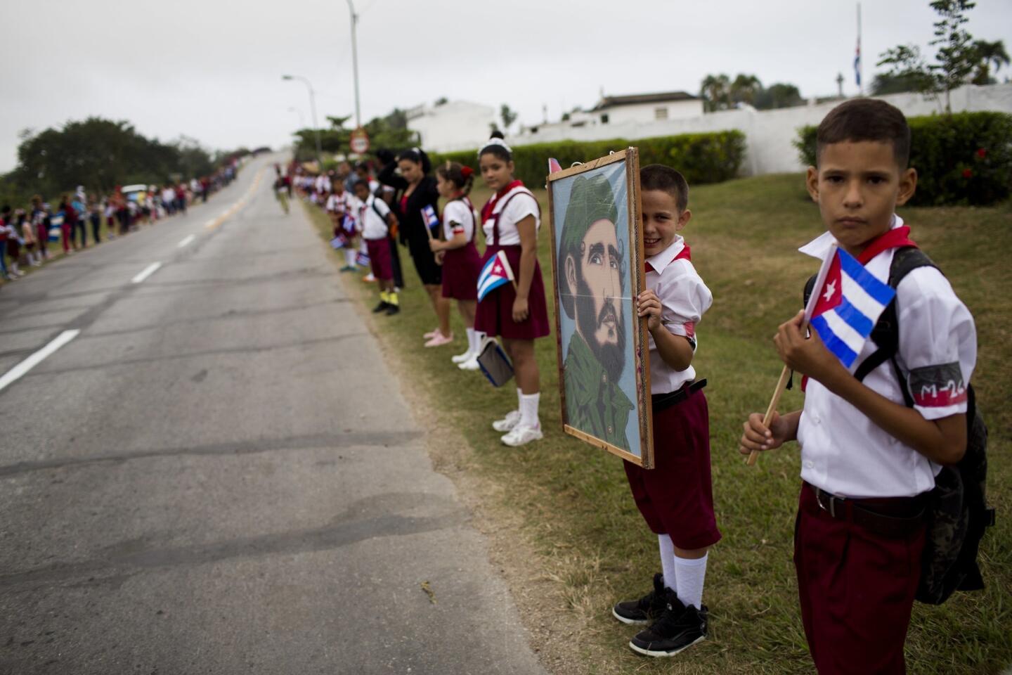 Decenas de escolares, uno con un retrato de Fidel Castro, esperan a lo largo de un camino al paso del convoy militar con las cenizas del líder cubano Fidel Castro cerca del pueblo de Baire, en el este de Cuba, el sábado 3 de diciembre de 2016. (AP Foto/Rodrigo Abd)