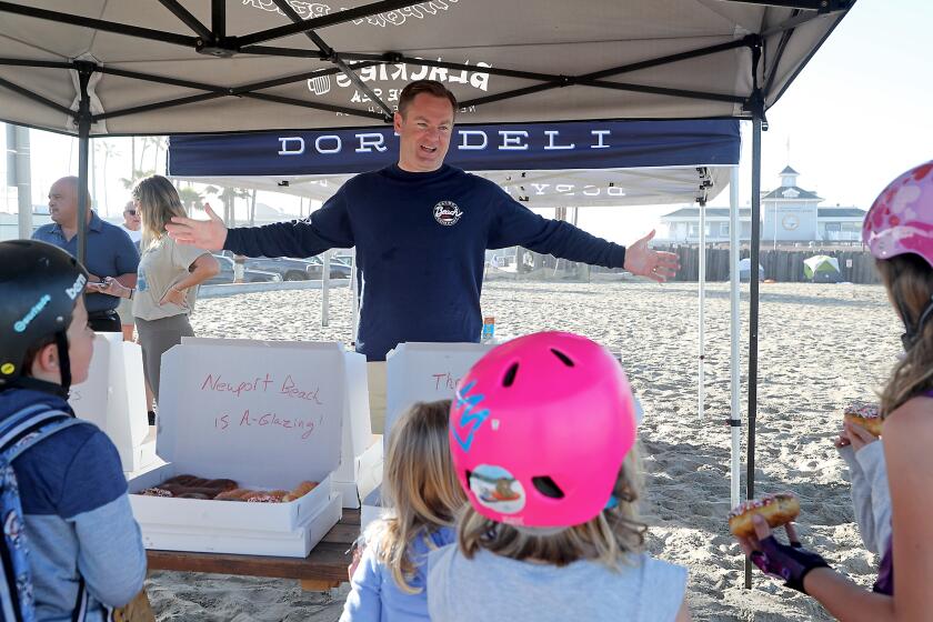 Newport Beach councilman Will O'Neill, center, speaks to Newport Elementary School students on their way to class as he gives out donuts on the beach in front of Dory Deli on Friday morning. April 30, 2021 marks the one-year anniversary of when Gov. Gavin Newsom shutdown the beaches in Newport Beach due to the COVID-19 pandemic.