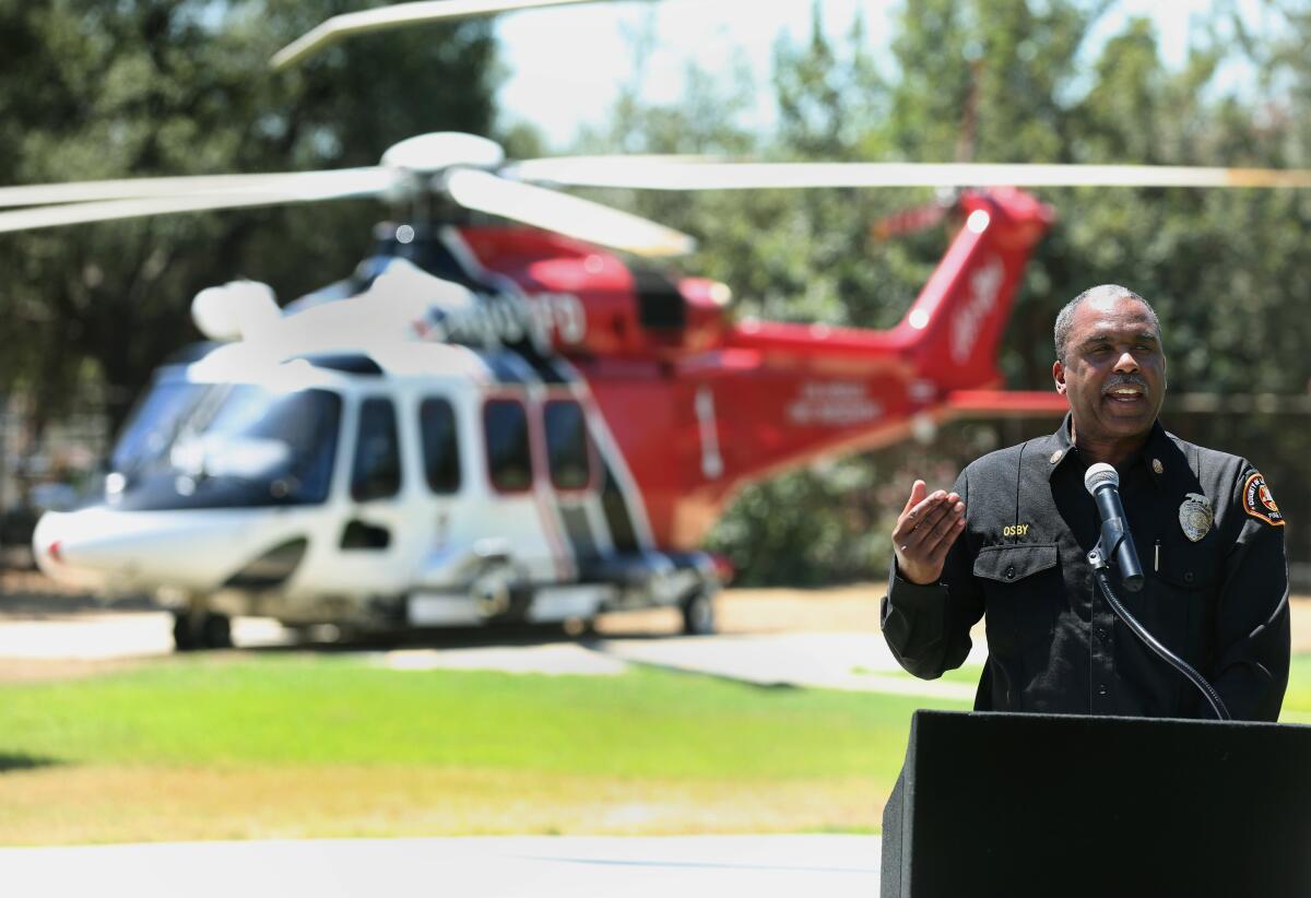 Los Angeles County Fire Chief Daryl Osby speaks with a helicopter as a backdrop