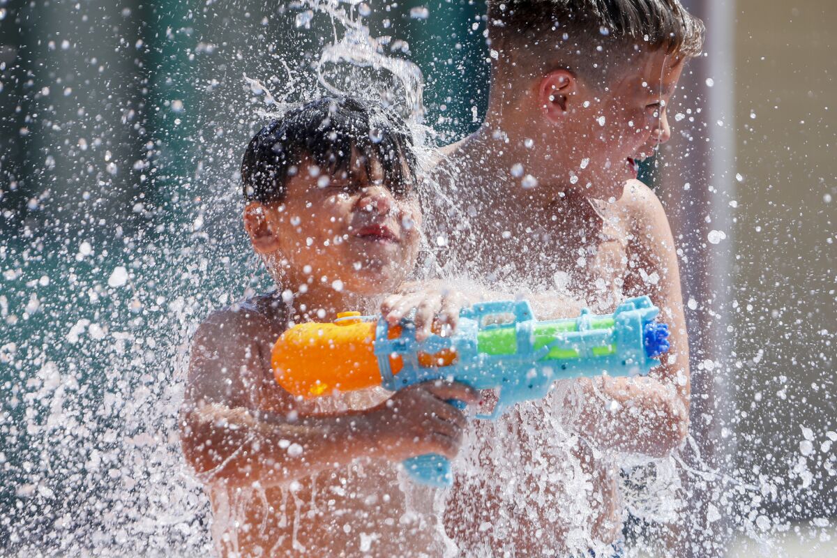 A boy holding a water gun and another boy are sprayed by water in a play area
