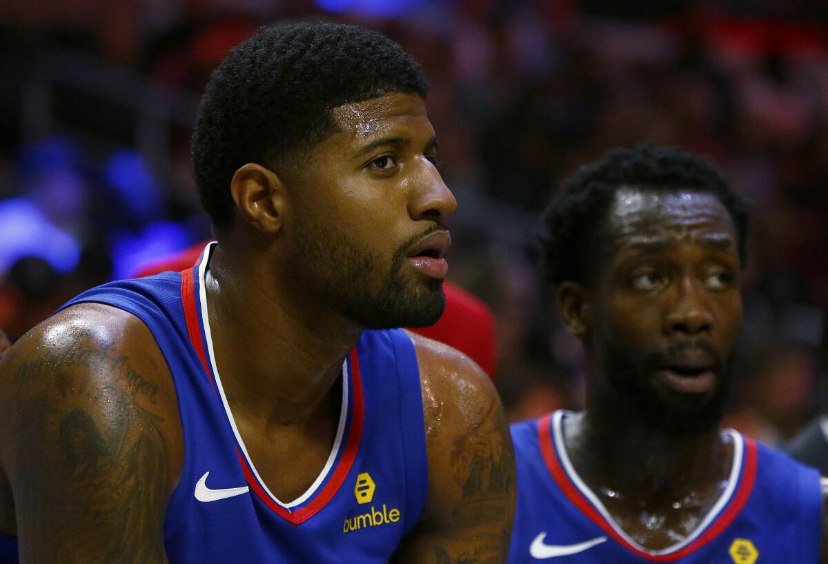 Clippers teammates Paul George, left, and Patrick Beverley watch a game from the sideline earlier this season.