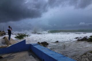 ARCHIVO - Una mujer toma fotos de las olas que chocan contra un rompeolas mientras el huracán Ian pasa por George Town, en la isla Gran Caimán, el 26 de septiembre de 2022. (AP Foto/Kevin Morales, Archivo)