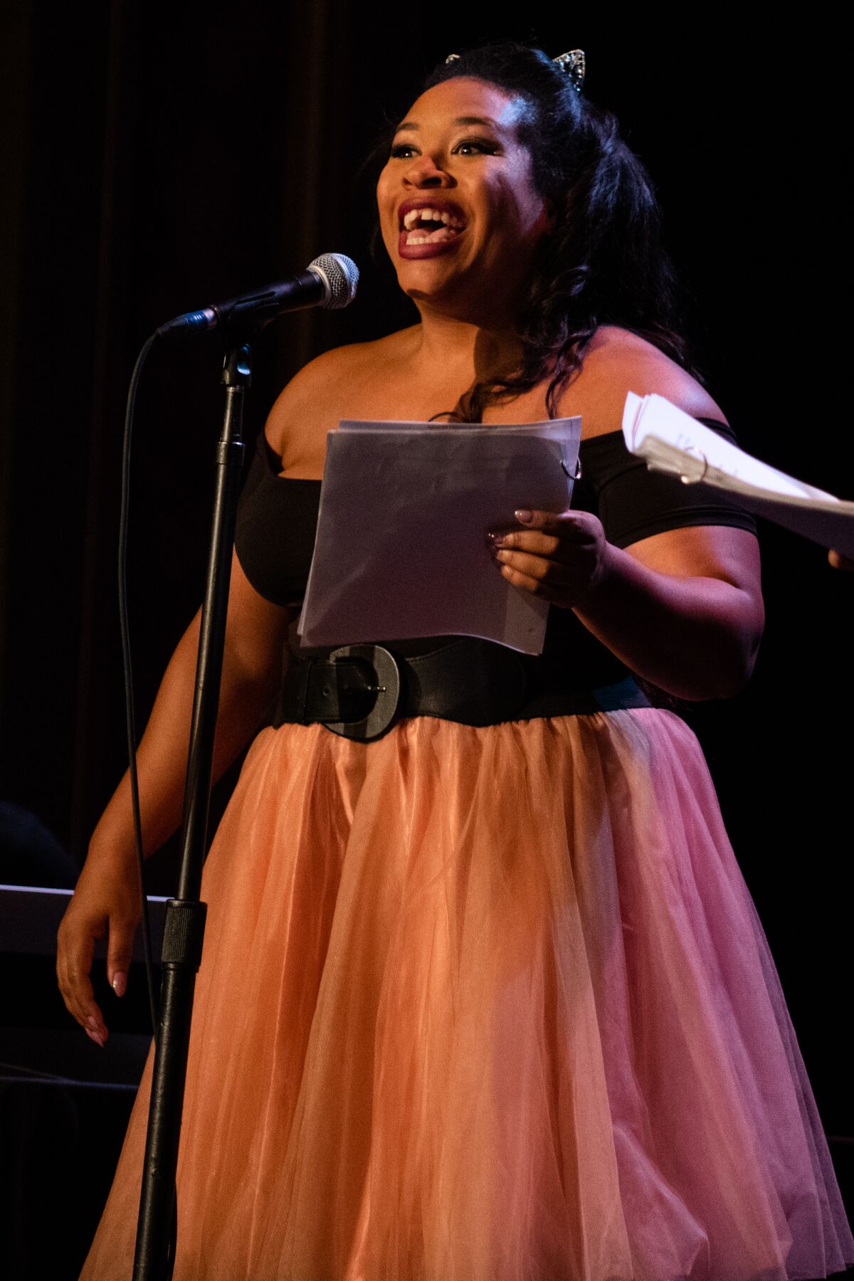 A woman at a microphone holds a script.