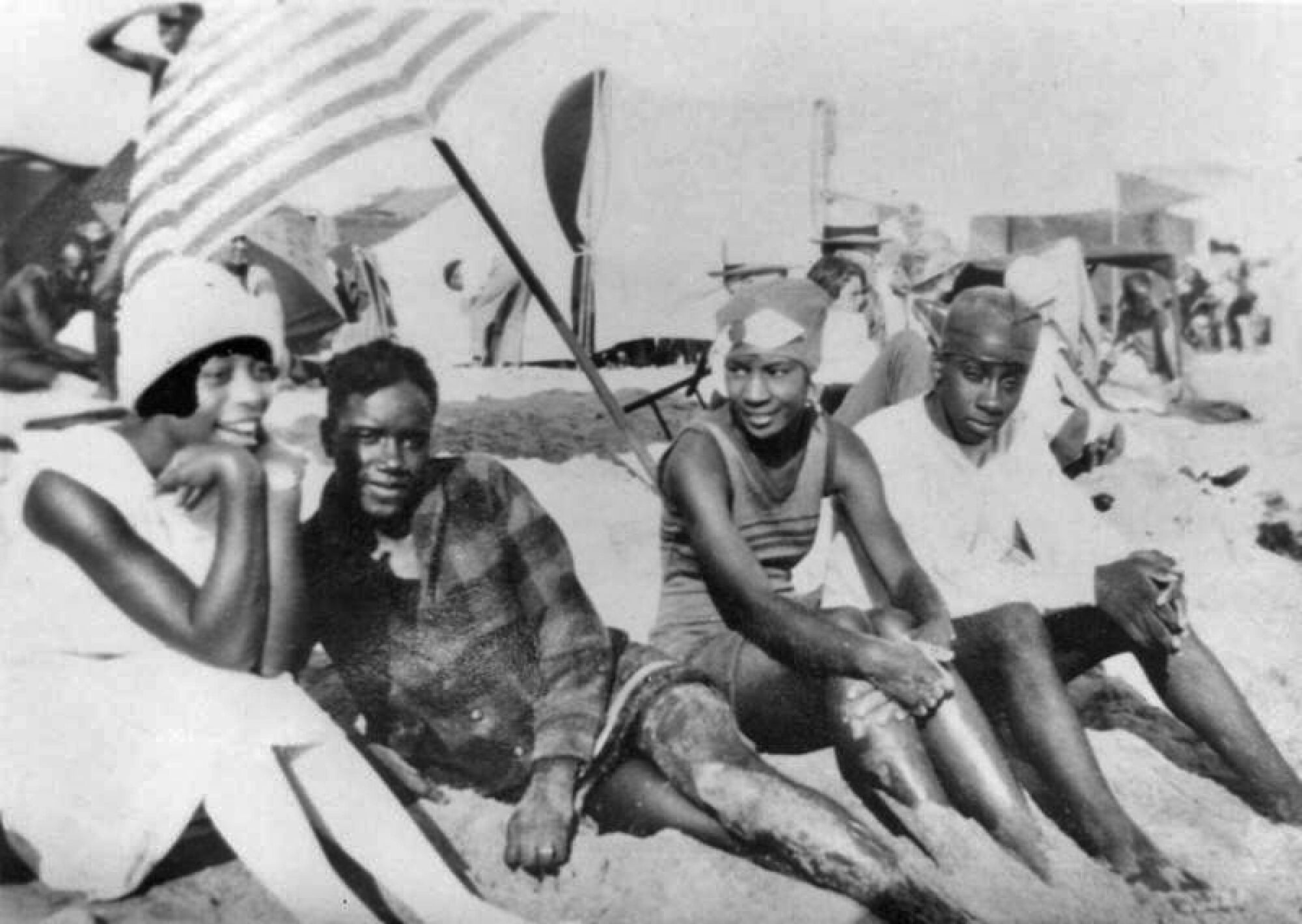 Four young Black people sit on the sand in the segregated section of Santa Monica Beach in 1926. 