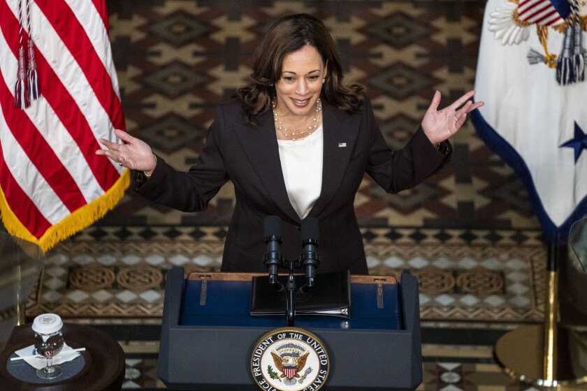 Vice President Kamala Harris raises her hands while speaking at a lectern.