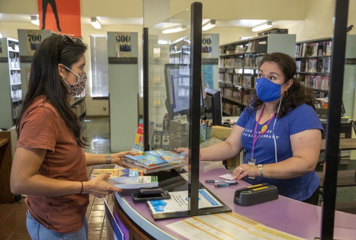 A librarian hands a book to someone through plexiglass.