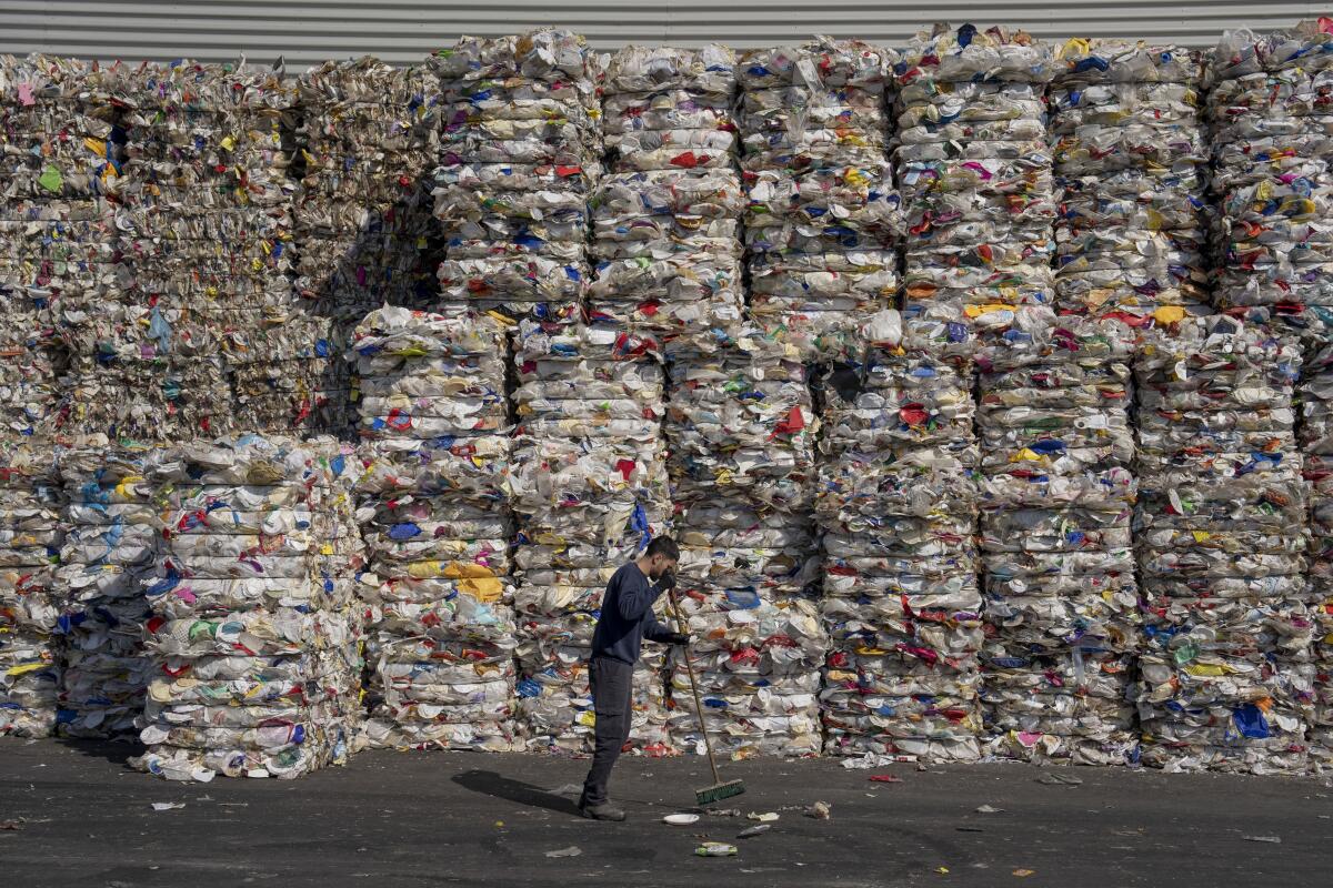 Un empleado de una planta de reciclaje GreenNet limpia el piso junto a grandes pilas de plástico 