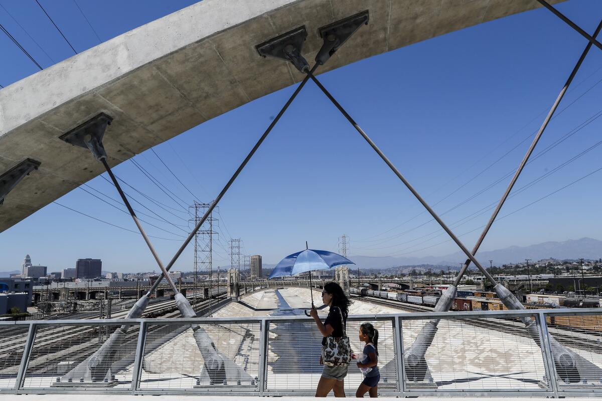 A woman and girl walk on the 6th Street Viaduct using an umbrella for shade.