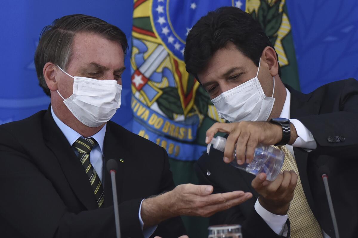 Brazil's Health Minister Luiz Henrique Mandetta, right, gives antibacterial gel to President Jair Bolsonaro
