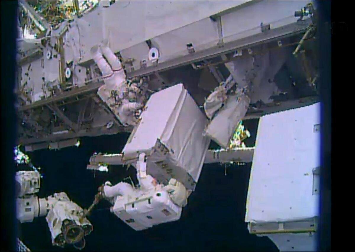 A NASA TV image shows astronauts Mike Hopkins, left, and Rick Mastracchio position a spare ammonia pump during a spacewalk outside the International Space Station.