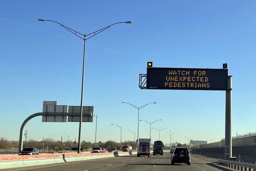 FILE - An electronic sign flashes "Watch for unexpected pedestrians," Dec. 20, 2022, on the highway next to the fenced US-Mexican border just east of downtown El Paso, Texas, next to one of the three bridges that connect the Texas city with the sprawling metropolis of Juarez, Mexico. The Supreme Court soon could find itself with easy ways out of two high-profile cases involving immigration and elections, if indeed the justices are looking to avoid potentially messy, divisive decisions. (AP Photo/Giovanna Dell'Orto, File)