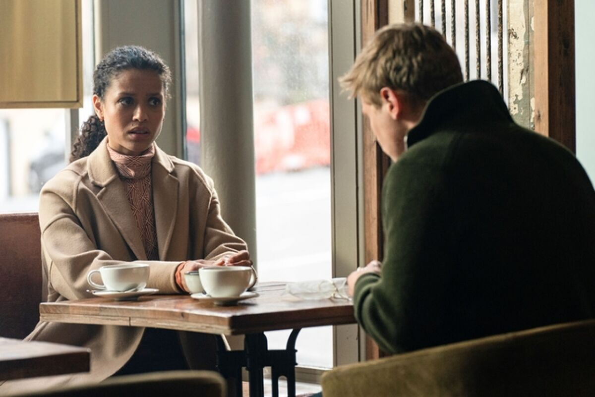A woman looking pensive in a brown coat, having coffee with a man.