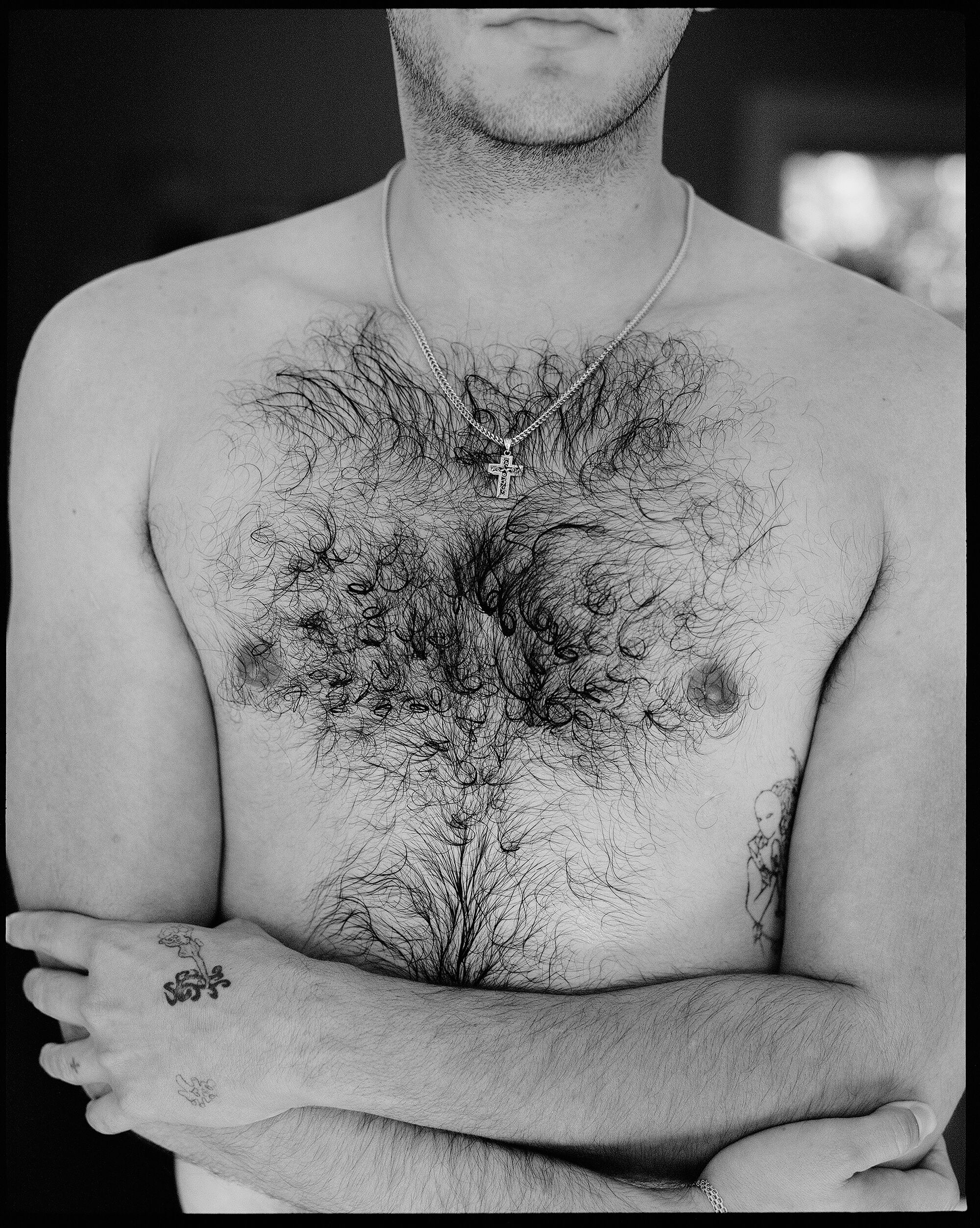 The hairy torso of a bare-chested man with crossed arms.