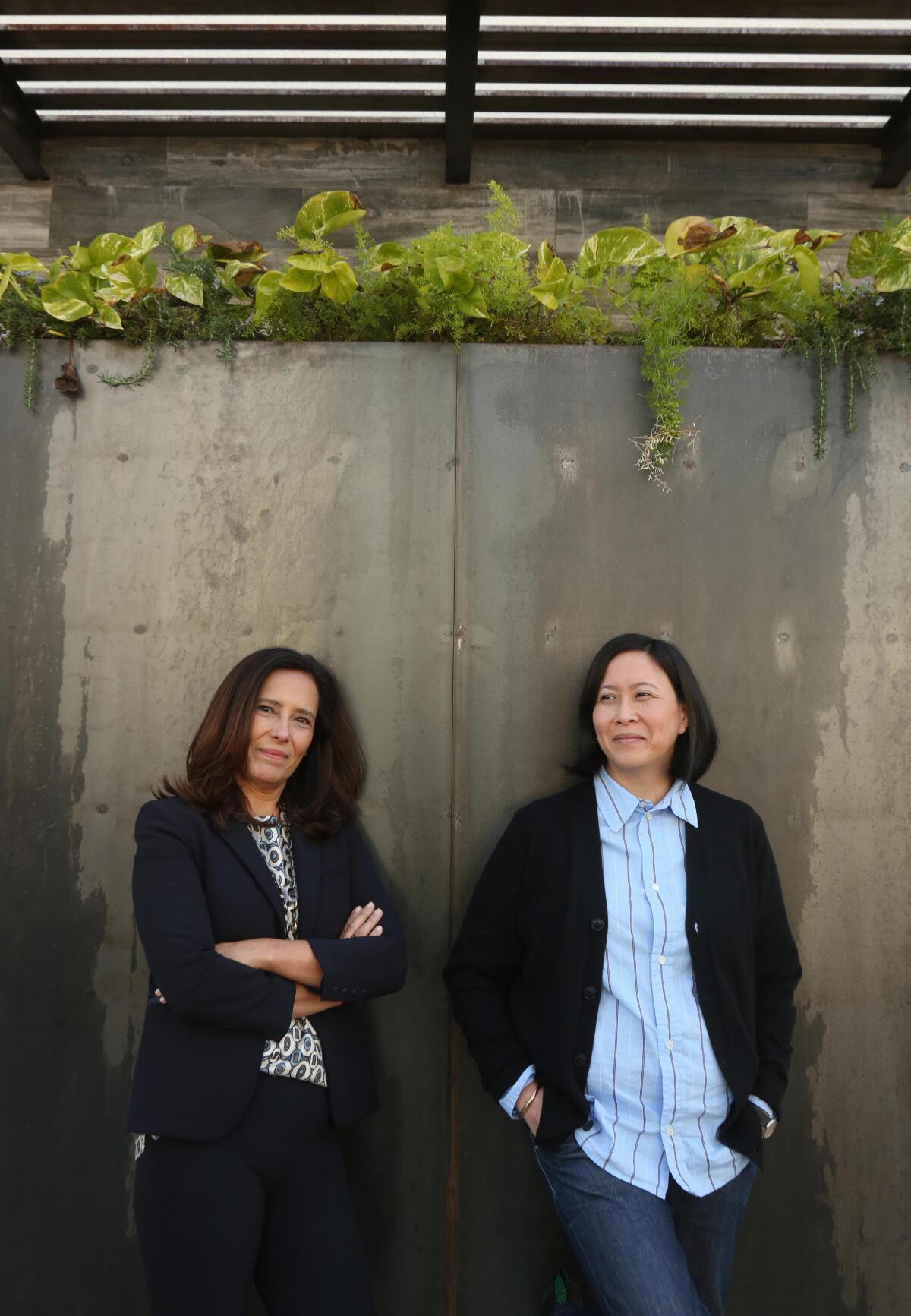 Two women pose beneath a concrete plant holder 